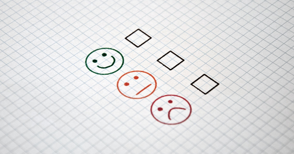 A drawing of a happy face, a neutral face and a sad face with a en empty tick box next to each