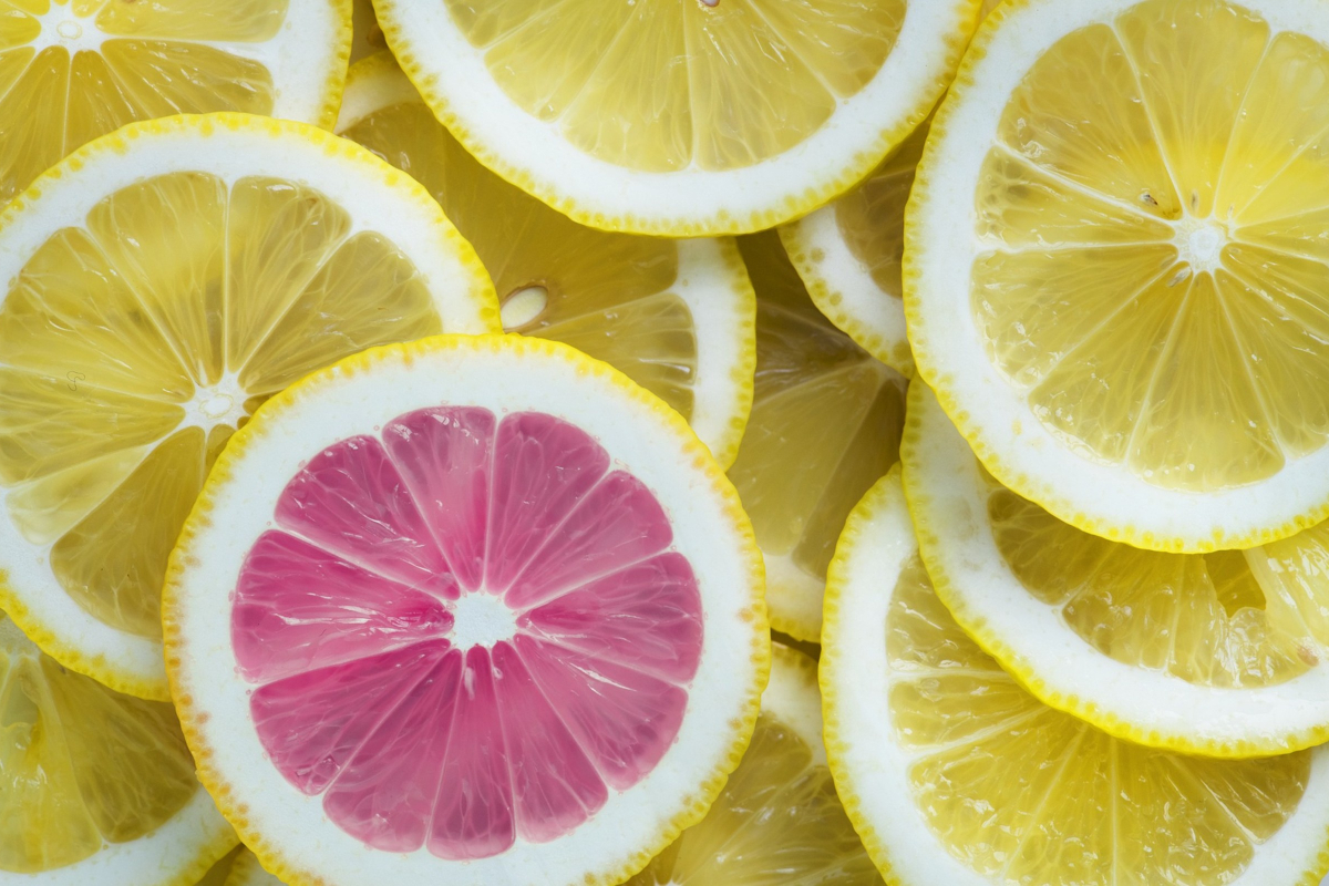 A slice of pink grapefruit amongst slices of lemon, highlighting the unique colour.
